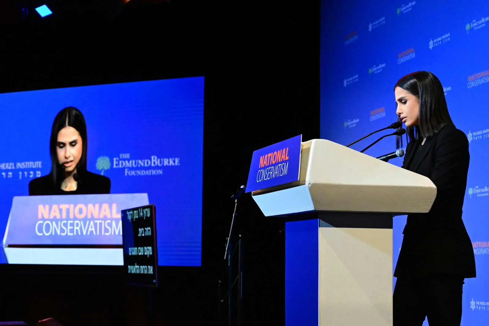 Maggie Tabibi at the NatCon lectern and on the screen behind her